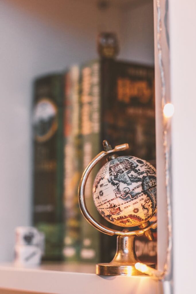 A cozy bookshelf featuring a vintage globe and warm string lights, creating a nostalgic atmosphere.